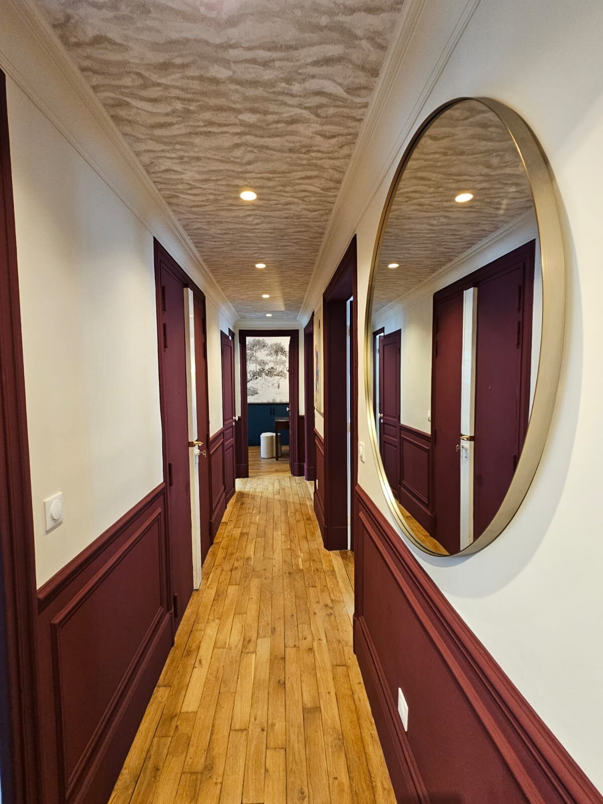 Couloir avec cimaises bordeaux et grand miroir rond doré