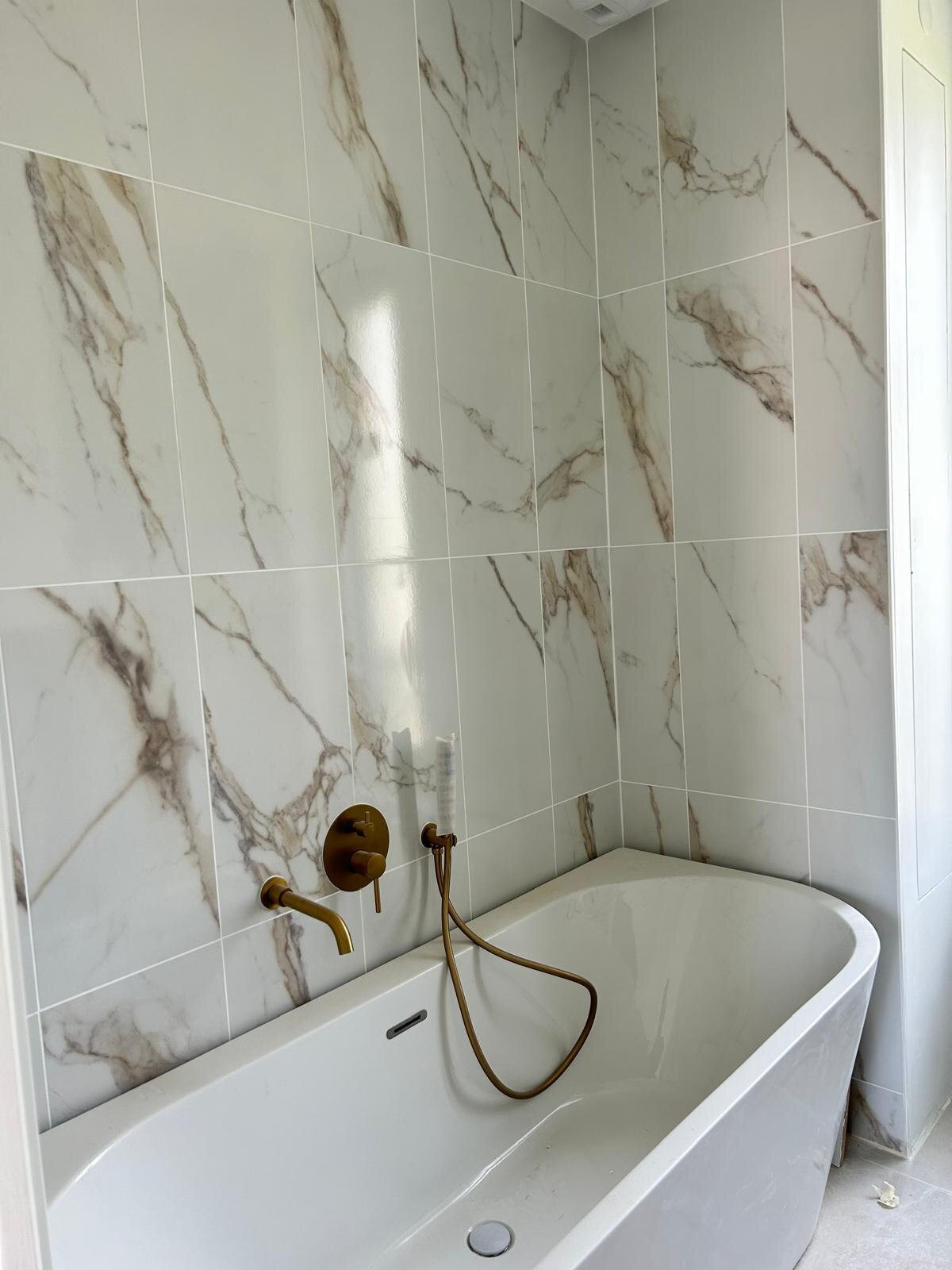 Salle de bain avec baignoire îlot, faïence marbrée et robinetterie laiton